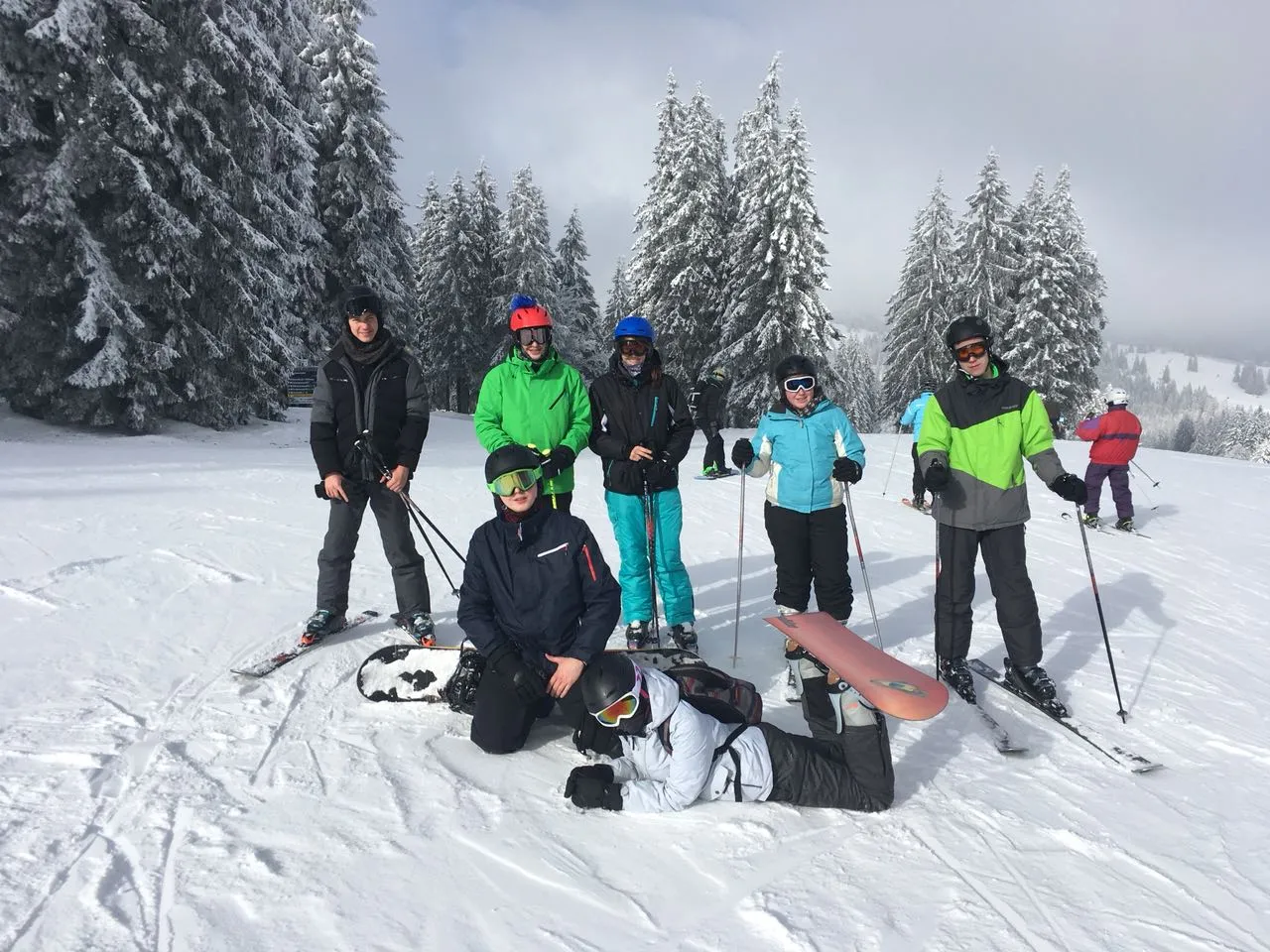 Kleine Gruppe Skifahrer stehend, im Vordergrund zwei Snowboardfahrer 